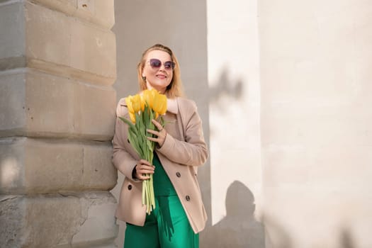 Woman holding yellow tulips, leaning against stone wall. Women's holiday concept, giving flowers