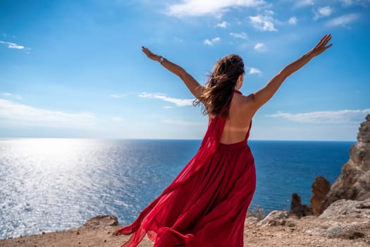 A woman in a red dress stands on a cliff overlooking the ocean. The scene is serene and peaceful, with the woman's dress adding a touch of elegance to the landscape