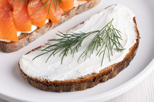 Rye sandwich with cream cheese and salmon on white wooden table.