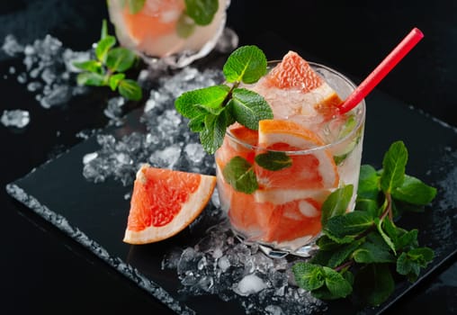 Refreshing grapefruit cocktail with ice and mint on a black background.