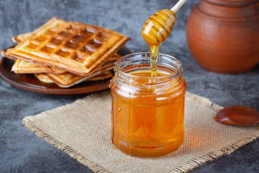 Honey in jar with honey dipper and belgian waffles.