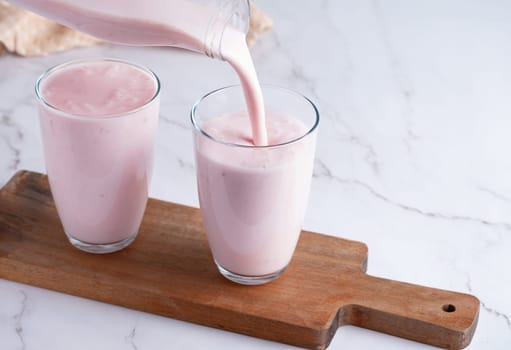 Pouring homemade fruit kefir, buttermilk or yogurt with probiotics. Yogurt flowing from glass bottle on light background. Probiotic cold fermented dairy drink. Trendy food and drink. Copy space.