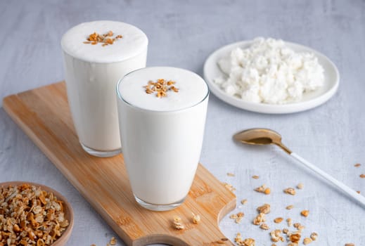 Kefir, buttermilk or yogurt, cottage cheese with granola. Yogurt in glass on white wooden background. Probiotic cold fermented dairy drink. Gut health, fermented products, healthy gut flora concept. Copy space.