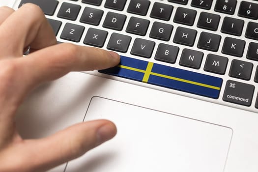 Online International Business concept: Computer key with the Sweden on it. Male hand pressing computer key with Sweden flag.