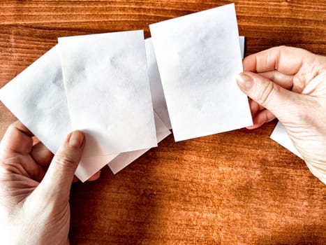 Woman Holding Small White Papers Over Wooden Surface. Hands presenting several small white papers