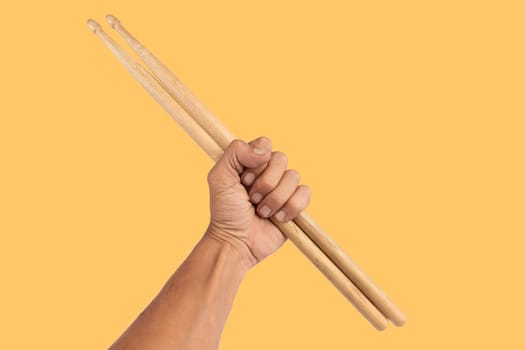 Black male hand holding wooden Drum sticks isolated on yellow background. High quality photo