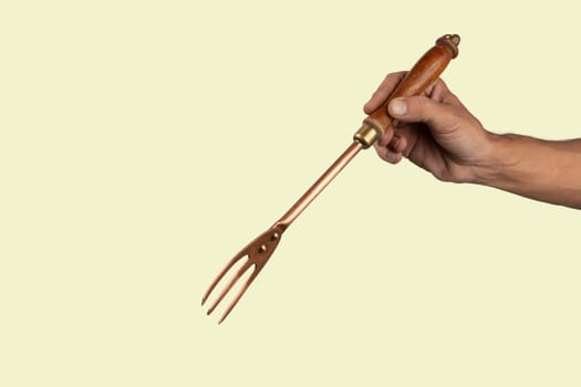 Black male hand holding a vintage brass meat fork on green background. High quality photo