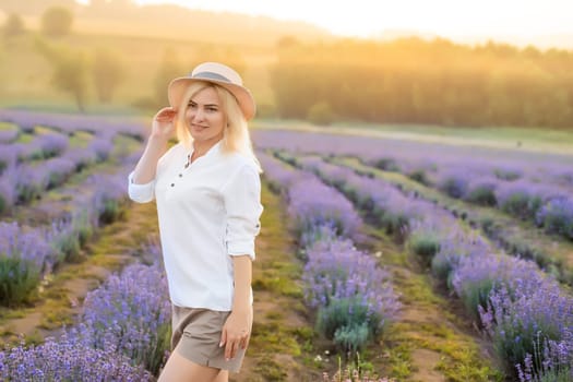 Young blond woman traveller wearing straw hat in lavender field surrounded with lavender flowers