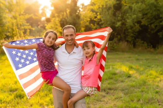 Happy family with the American flag in a wheat field at sunset. Independence Day, 4th of July