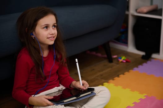 Adorable smart little child girl holding digital tablet and white stylus, learning online, doing homework, drawing pictures, watching cartoons or listening to online webinar class. Kids and technology