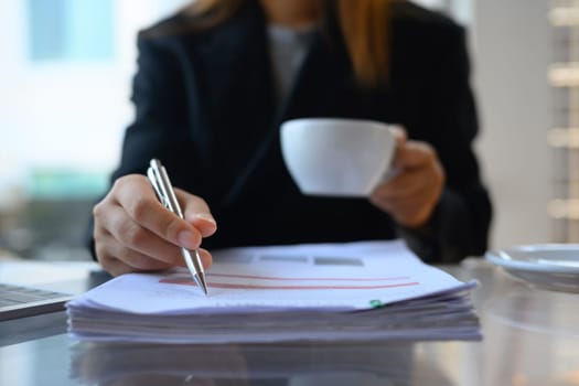 Cropped shot businesswoman working with document and drinking coffee at her workplace.