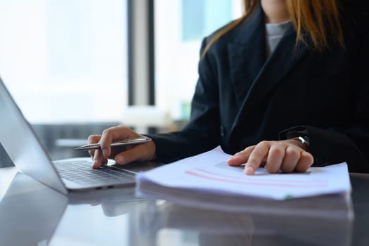 Young business woman working with laptop and reading financial report at office desk.