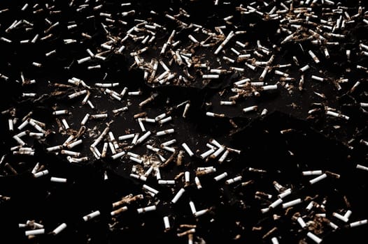 Lots of cigarette butts on black background, Dirty backdrop for banner about the dangers of smoking and toxicity.