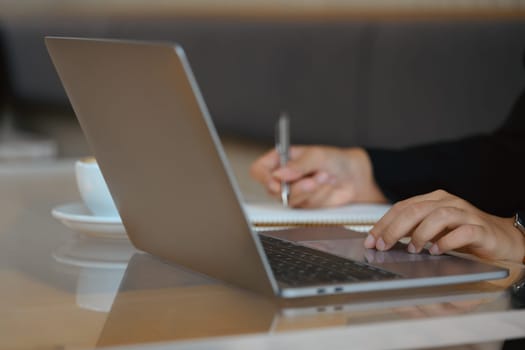 Unrecognizable businesswoman hands typing on laptop and making notes. Close up view.