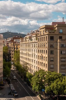 Cityscape showcasing classic architecture and green-lined streets in Barcelona under a cloudy sky.