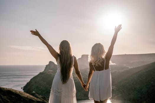 Two women are standing on a hill overlooking the ocean. They are holding hands and looking out at the water. The scene is peaceful and serene, with the sun shining brightly in the background