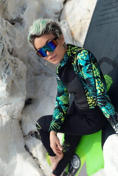 beautiful sup surfer girl in a wetsuit on the ocean shore against a beautiful blue sky poses sexually with a paddle