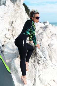 beautiful sup surfer girl in a wetsuit on the ocean shore against a beautiful blue sky poses sexually with a paddle