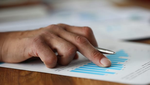 Focus on male hands holding metallic ball pen and pointing at important graphs of statistics data. Financial forecast of new start-up. Stock Exchange, Securities Market concept. Blurred background