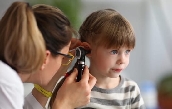 Pediatrician examines ear of sick child in office of hospital background. Otitis Prevention Concept