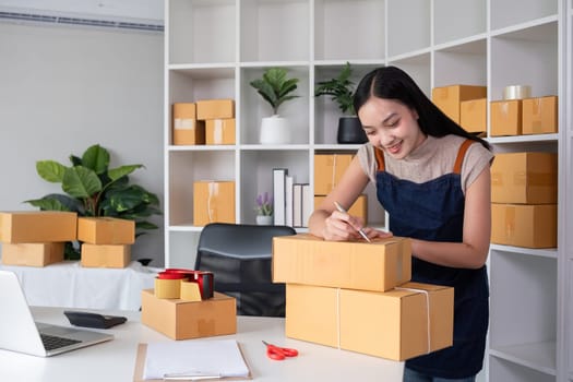 SME business entrepreneurs small in Asia Write shipping information on a cardboard box in home office. Small business operators preparing to ship to customer.