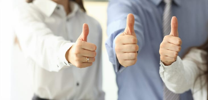 Focus on tender female and male hands showing big thumb up and posing at modern workplace. Businesspeople working in office together. Teamwork concept