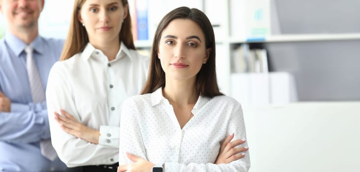 Portrait of smiling lady standing with businesspeople together. Joyful businesswoman standing at modern workplace and looking at camera with calmness and gladness. Friendly teamwork concept