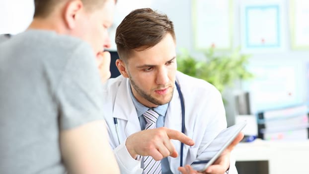 Portrait of concentrated doctor pointing to gadget with finger. Patient listening attentively to doc recommendations. Medical treatment concept. Blurred background