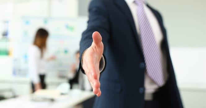 Focus on man stretching out to shake hands with colleague or boss. Younger managers working on new business strategy for corporate people. Company meeting concept. Blurred background
