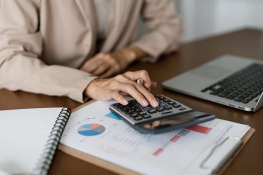 Businesswoman using a calculator to calculate numbers on a company's financial documents, she is analyzing historical financial data to plan how to grow the company. Financial concept.