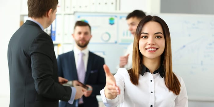 Portrait of pretty lady reaching tender arm to perform friendly gesture towards colleague or business manager. Beautiful female in classy bluse smiling at camera with joy. Company meeting concept