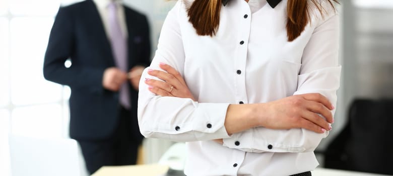 Close-up of gorgeous female standing in big modern office with crossed hands. Pretty woman discussing questionable subject with witty colleagues and managers. Company meeting concept