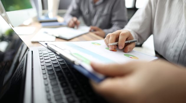 Group of people working with financial reports clipped to pad at workplace closeup