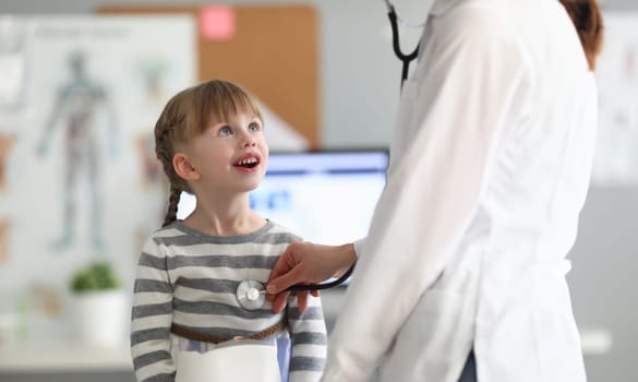 Doctor listens to smiling happy child with stethoscope in hospital office. Pediatrics Disease Concept