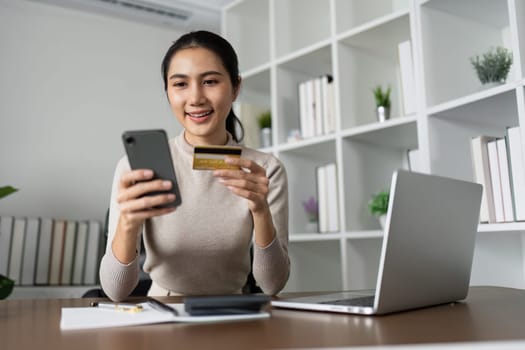 Woman using laptop computer and mobile phone holding credit card for shopping online.