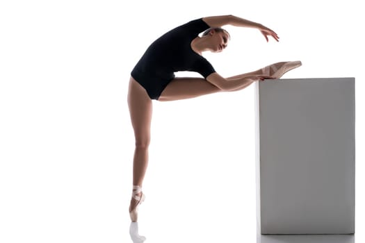 Studio image of ballerina putting her leg on cube while warming up