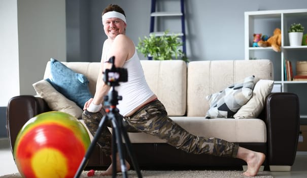 Happy Vlogger Doing Exercise for Legs in Apartment. Smiling Sportsman Recording Fitness Video on Digital Camcorder for Sport Vlog. Bearded Man Practice Aerobic Indoor for Muscular and Healthy Body