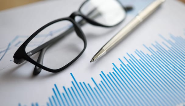 Silver pen with paper chart and glasses lie in office table closeup. Business education concept