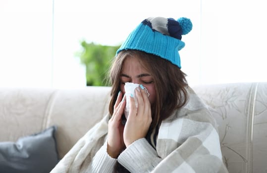 Woman stayed home on sick leave sitting on couch wipes snot with runny napkin portrait. Season disease concept