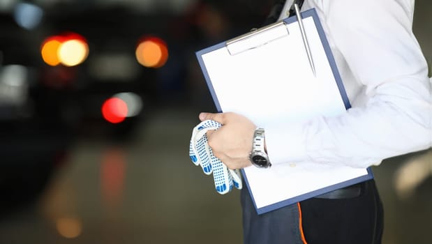 Focus on hands of engineer holding paper folder with technical description about autos and working gloves. Machinery repairman concept. Blurred background