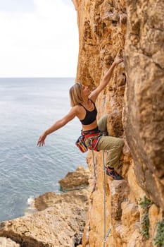 A woman is climbing a rock wall with a rope. The scene is set against a backdrop of the ocean