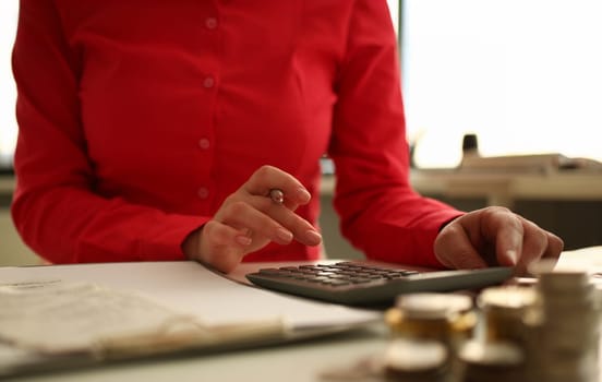 Focus on woman hand holding pen and taping calculator. Accountant sitting at table with papers and making business plan. Female accounting income or savings in office