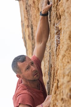 A man in a red shirt is climbing a rock wall. He is wearing a wristwatch and a black band