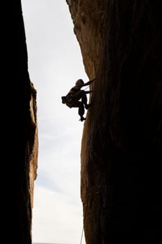 A person is climbing a rock wall in a cave. The person is wearing a backpack and is wearing a helmet