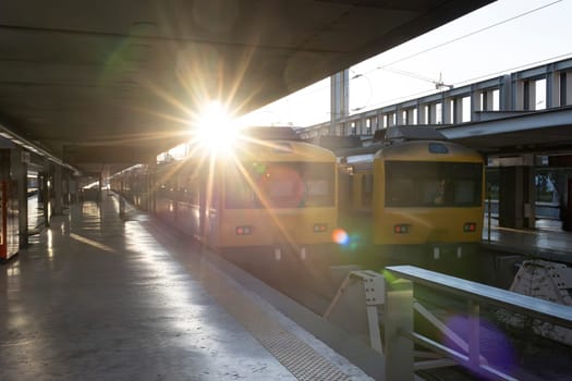 A train station with two yellow trains parked on the platform. The sun is shining brightly, creating a warm and inviting atmosphere