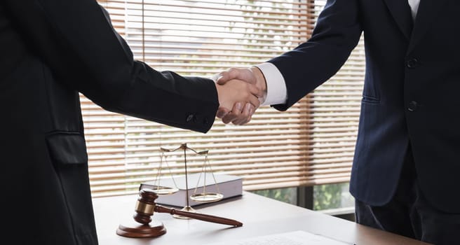 A lawyer and a businesswoman shake hands and reach an agreement on a cooperation contract document. In the lawyer's office and there is a hammer lying on the table..