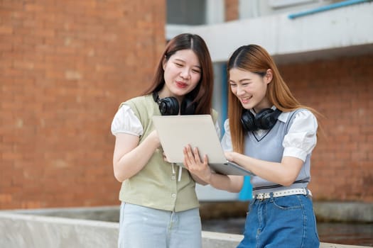 Two female college friends are chatting and exchanging ideas about their studies on laptops during their free time..