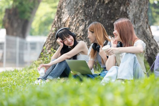 Happy Asian teenage female college students tutor together in the garden outside the university classroom. Female students happily help each other with their homework..