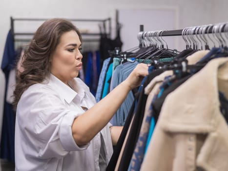 A fat woman in a plus size store chooses clothes while sorting through hangers
