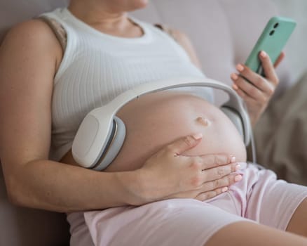 A pregnant woman turns on music for her child on a smartphone. Headphones on the tummy